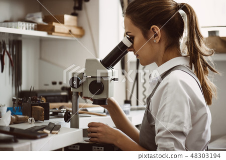 Utmost precision. Close up portrait of female jeweler looking at the new jewelery product through 48303194