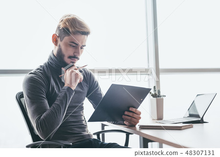 Pensive stylish businessman sitting at office desk Pensive stylish businessman sitting at office desk 48307131