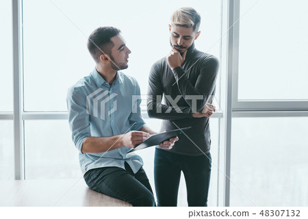 Two focused male co-workers deep in discussion together, while standing in a modern office 48307132