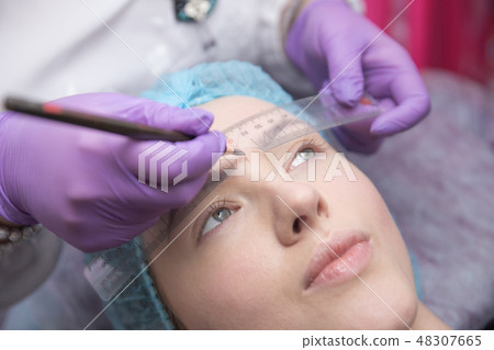 make-up for eyebrows of beautiful woman with thick brows in beauty salon. Closeup beautician doing make-up for eyebrows of beautiful woman with thick brows in beauty salon. Closeup beautician doing 48307665