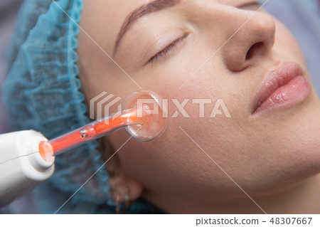 Receiving electric darsonval facial massage procedure at salon Receiving electric darsonval facial massage procedure at salon 48307667