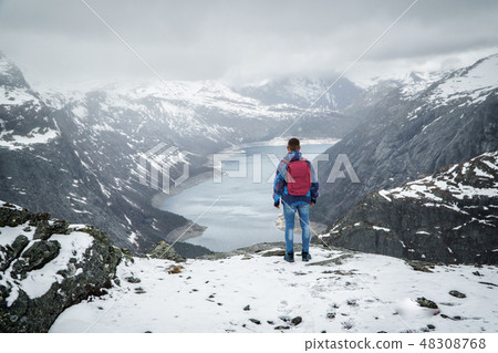 Man traveller with backpack standing back on edge and looking at scenery mountain landscape under Man traveller with backpack standing back on edge and looking at scenery mountain landscape under 48308768