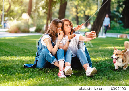 Two female friend sitting in the park have a rest take a selfie Two female friend sitting in the park have a rest take a selfie 48309400