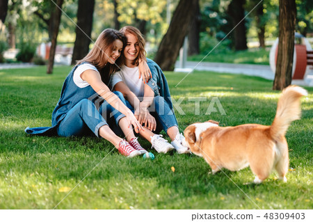 Two female friend in the park play with little dog Two female friend in the park play with little dog 48309403