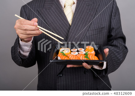 Hands of mature Asian businessman holding sushi rolls against gr 48312609