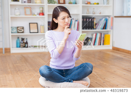 認為觀看一個智能手機的婦女在屋子裡 認為觀看一個智能手機的婦女在屋子裡 48319873