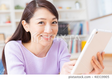 觀看一台片劑計算機的婦女在屋子裡 觀看一台片劑計算機的婦女在屋子裡 48319905