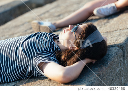 Portrait of beautiful girl relaxing lying on the walls  facing the sun 48320468