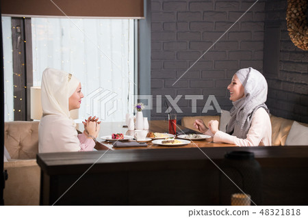 Two young Muslim women chatting at a table in a cafe 48321818