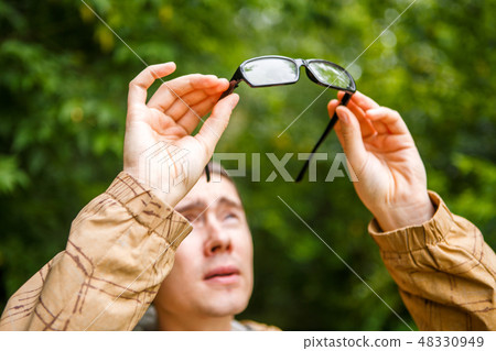 Photo of man holding glasses against trees Photo of man holding glasses against trees 48330949