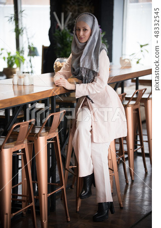 A young muslim woman sitting on a bar chair in a cafe A young muslim woman sitting on a bar chair in a cafe 48332545