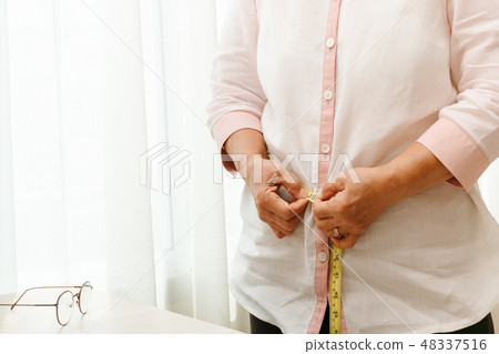Senior woman measuring her waist by measuring tape 48337516