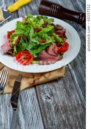 Salad leaves with sliced roast beef and sun-dried cherry tomatoes on wooden background Salad leaves with sliced roast beef and sun-dried cherry tomatoes on wooden background 48337552