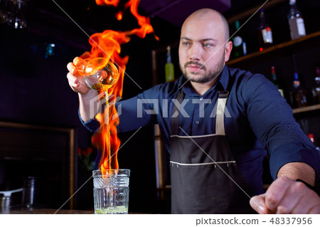 Fiery show at the bar. The bartender makes hot alcoholic cocktail and ignites bar. Bartender Fiery show at the bar. The bartender makes hot alcoholic cocktail and ignites bar. Bartender 48337956