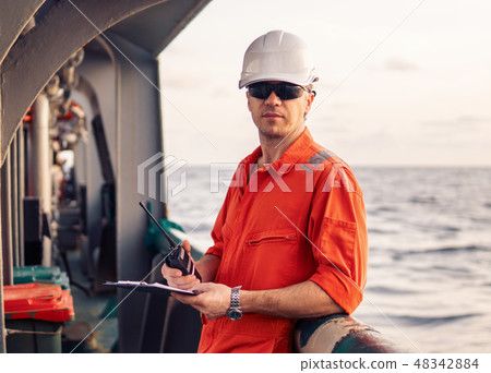 Deck Officer on deck of offshore vessel holds VHF walkie-talkie radio Deck Officer on deck of offshore vessel holds VHF walkie-talkie radio 48342884