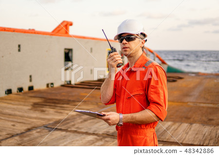 Deck Officer on deck of offshore vessel holds VHF walkie-talkie radio 48342886