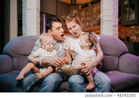 Young family with children eating popcorn on the couch. 48343285
