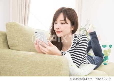 A woman using a smartphone on a sofa A woman using a smartphone on a sofa 48352702