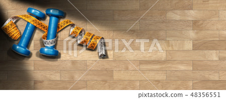 Dumbbells and tape measure on wooden gym floor Dumbbells and tape measure on wooden gym floor 48356551