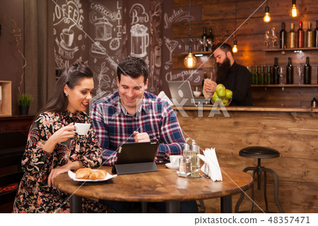 Happy couple using digital tablet while having coffee at restaurant Happy couple using digital tablet while having coffee at restaurant 48357471