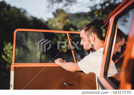 A young man getting out of a car on a roadtrip through countryside. 48357576