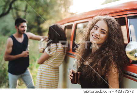 A group of friends standing outdoors on a roadtrip through countryside, holding bottles. 48357578