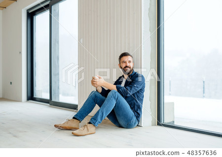 A mature man with cup of coffee sitting on the floor, furnishing new house. A mature man with cup of coffee sitting on the floor, furnishing new house. 48357636