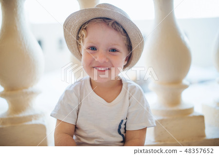 A front view of small toddler boy sitting in front of concrete railing on summer holiday. A front view of small toddler boy sitting in front of concrete railing on summer holiday. 48357652
