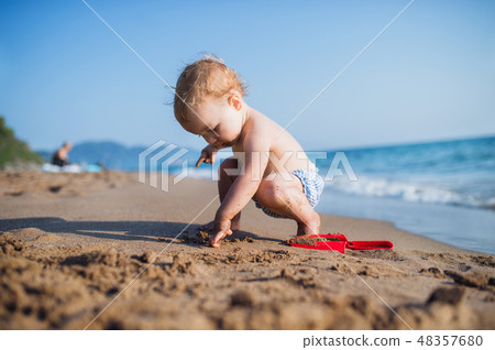 A small toddler girl sitting on beach on summer holiday, playing. A small toddler girl sitting on beach on summer holiday, playing. 48357680