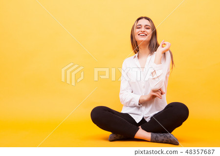 Beautiful young woman smiling while sitting down on yellow background Beautiful young woman smiling while sitting down on yellow background 48357687