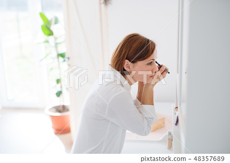 A young woman putting on a make-up in the morning in a bathroom. A young woman putting on a make-up in the morning in a bathroom. 48357689