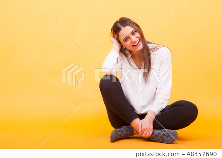 Beautiful young woman sitting down and smiling over yellow background 48357690