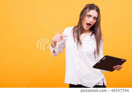 Portrait of happy girl wearing a white shirt showing towards tablet over yellow background 48357704