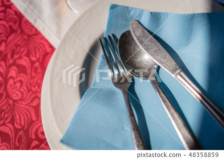 Fork, knife and spoon on a blue napkin on a plate Fork, knife and spoon on a blue napkin on a plate 48358859
