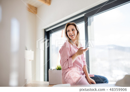 A young woman with smartphone moving in new home, sitting on table. A young woman with smartphone moving in new home, sitting on table. 48359906