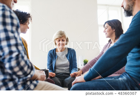 Men and women sitting in a circle and holding hands during group therapy. 48360307
