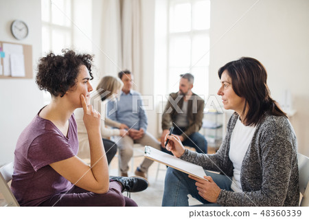Senior counselor with clipboard talking to a woman during group therapy. 48360339