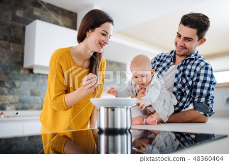 A young family at home, a man holding a baby and a woman feeding her. A young family at home, a man holding a baby and a woman feeding her. 48360404