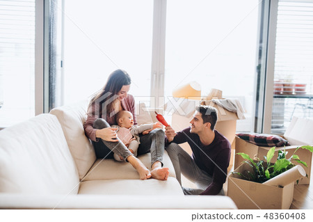 A portrait of young couple with a baby and cardboard boxes moving in a new home. A portrait of young couple with a baby and cardboard boxes moving in a new home. 48360408