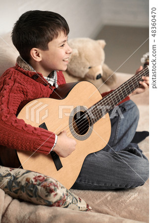 boy plays with an acoustic guitar, sits on  sofa 48360470