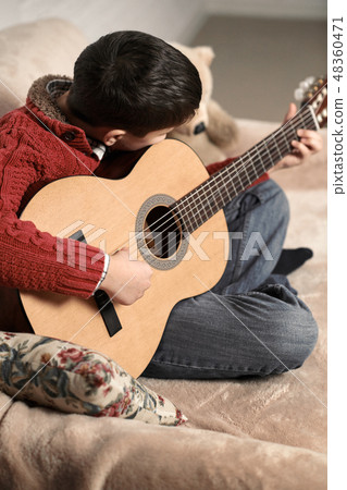boy plays with an acoustic guitar, sits on  sofa 48360471
