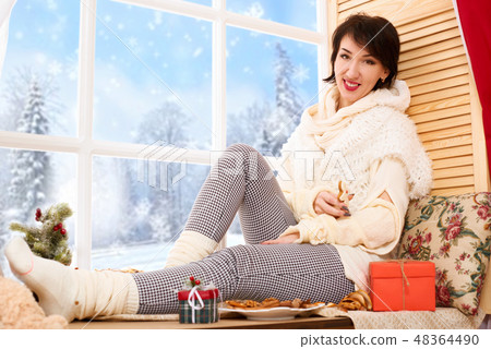 Woman sitting on window sill - sunny day in winter Woman sitting on window sill - sunny day in winter 48364490