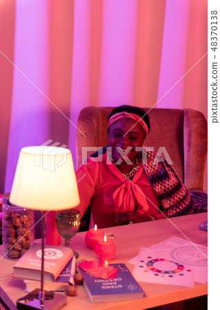 African american plump fortune-teller in ethnic adornments sitting at the table 48370138