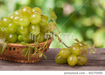 green grapes in a wicker basket on wooden table with blurred background green grapes in a wicker basket on wooden table with blurred background 48370999