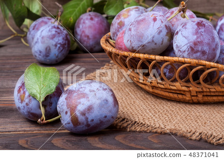 plum in a wicker basket on the wooden background with sackcloth 48371041