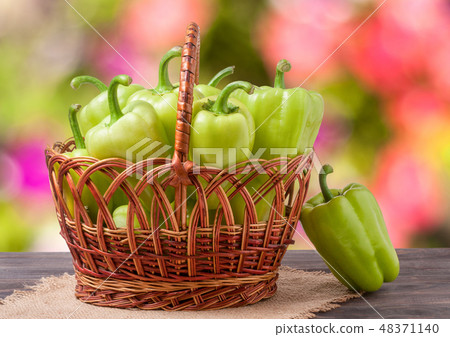 green bell peppers in a wicker basket on  wooden table with  blurred background 48371140