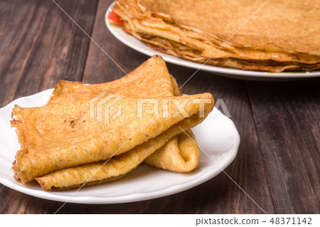 thin pancakes on a white plate with wood background 48371142