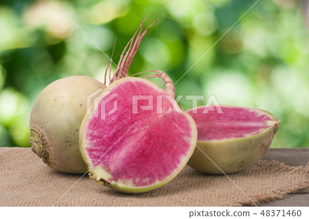 One whole and sliced watermelon radish on a wooden table with blurred garden background 48371460