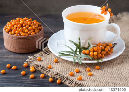 Tea of sea-buckthorn berries with a sprig on sackcloth and wooden background Tea of sea-buckthorn berries with a sprig on sackcloth and wooden background 48371600