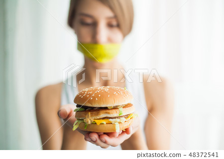 Diet. Young woman with duct tape over her mouth, preventing her to eat junk food. Healthy eating 48372541